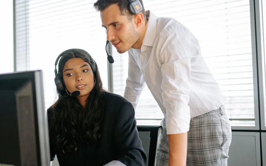 A colleague leaning in to review work on another person's screen at a desk.