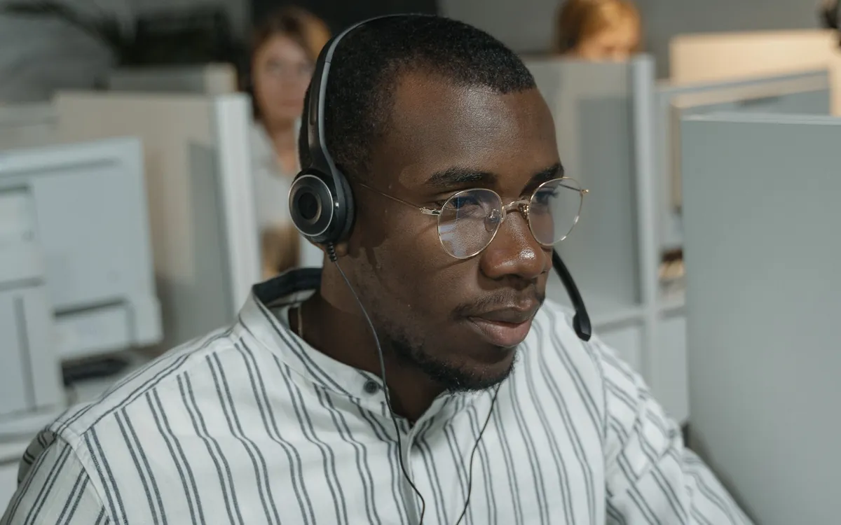 A support engineer at a workstation in an open-plan office, headset on.