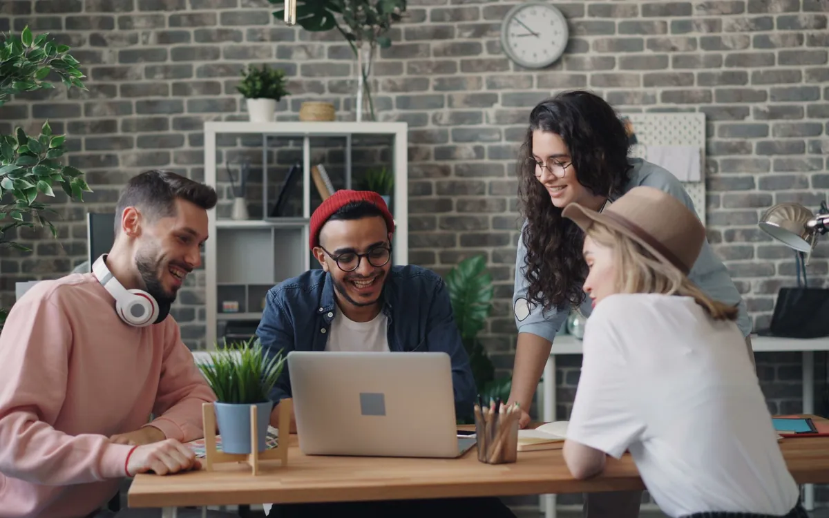 Four people gathered around a laptop at a shared table.